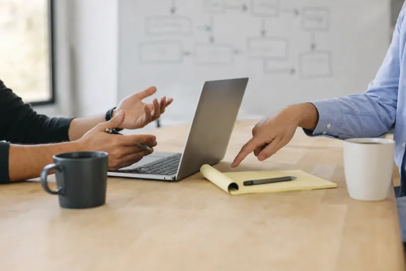 Two people at a meeting table with a laptop and a yellow legal pad, one pointing at the notes